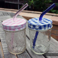 Two half pint Ball jars with pink and blue glass straws and gingham tumbler lids