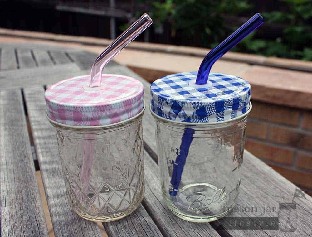 Two half pint Ball jars with pink and blue glass straws and gingham tumbler lids