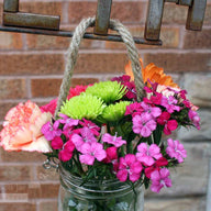 Thin rope handle on wide mouth quart Mason jar with flowers hanging on sign