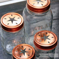 Copper star cutout lids and bands on 4 Ball Mason jars - a 4oz jelly jar, half pint jar, pint jar, and quart jar. Top view.