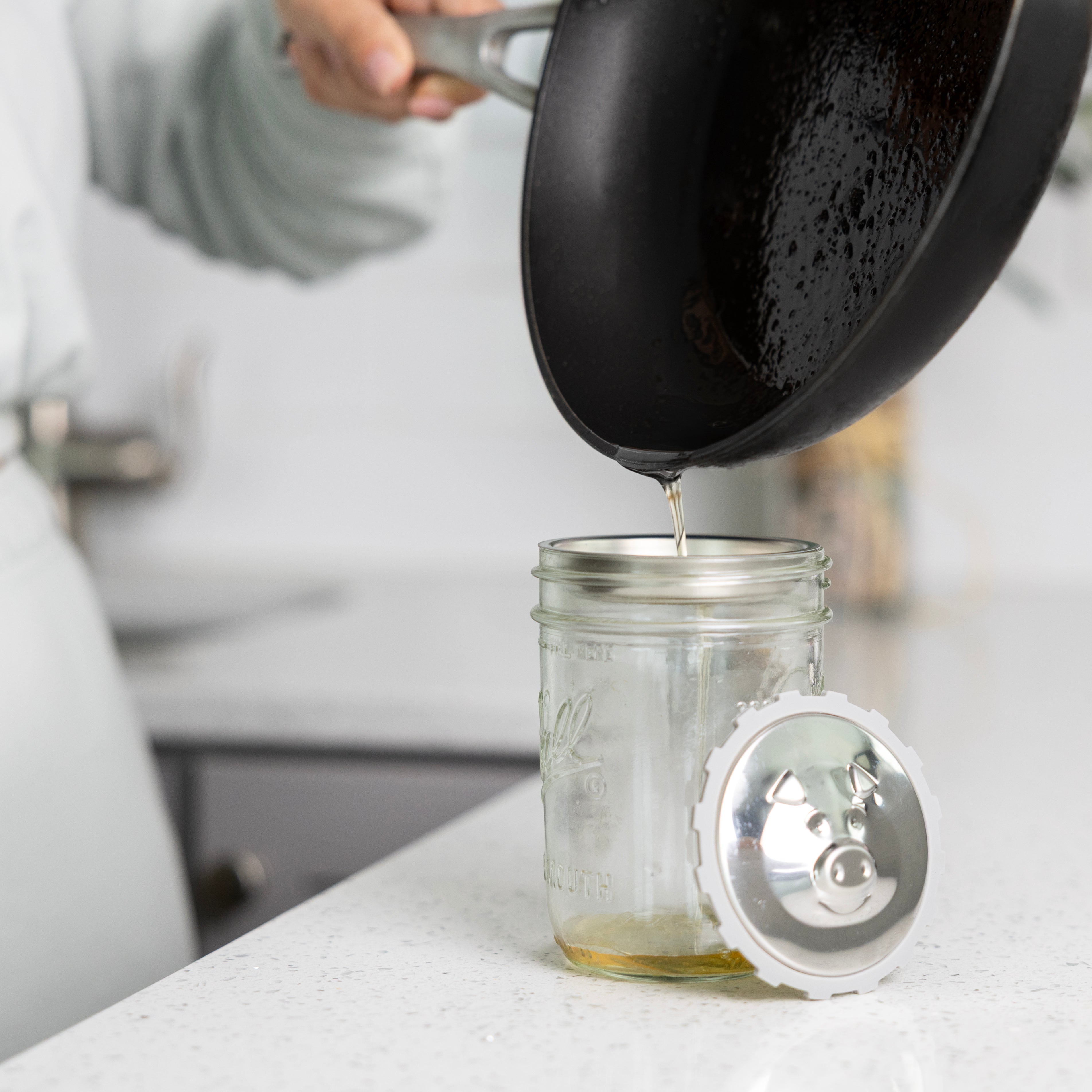 Bacon grease being poured into the strainer of the grease keeper, while on a Mason jar, catching the grease in the bottom.