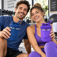 Couple in workout clothes holding Mason Jar Lifestyle 16oz glass protein shaker bottles with Deep Blue and Ultra Violet silicone sleeves and matching carry-loop lids.