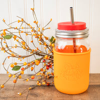 A tangerine colored Mason Jar sleeve on a wide mouth quart 32oz jar, with a fall colored branch of berries next to it.