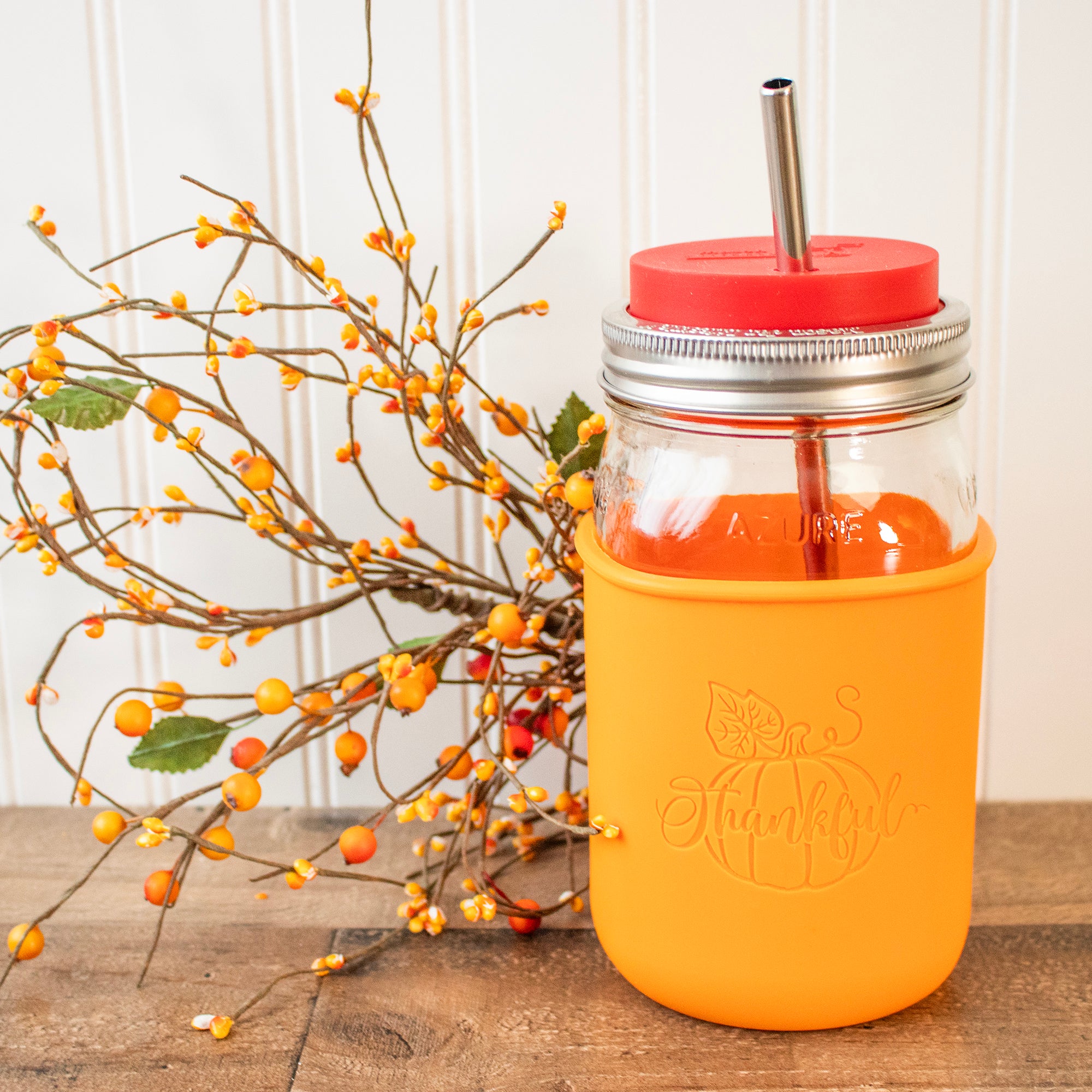 A tangerine colored Mason Jar sleeve on a wide mouth quart 32oz jar, with a fall colored branch of berries next to it.
