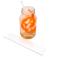 4 pack of short glass straws and the straw cleaner next to it, laying in front of a Mason jar full of water and oranges, with a glass straw in it.