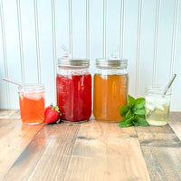 The same two Mason jars with liquor pour spouts, with additional glasses with cocktails in them with glass and metal straws.