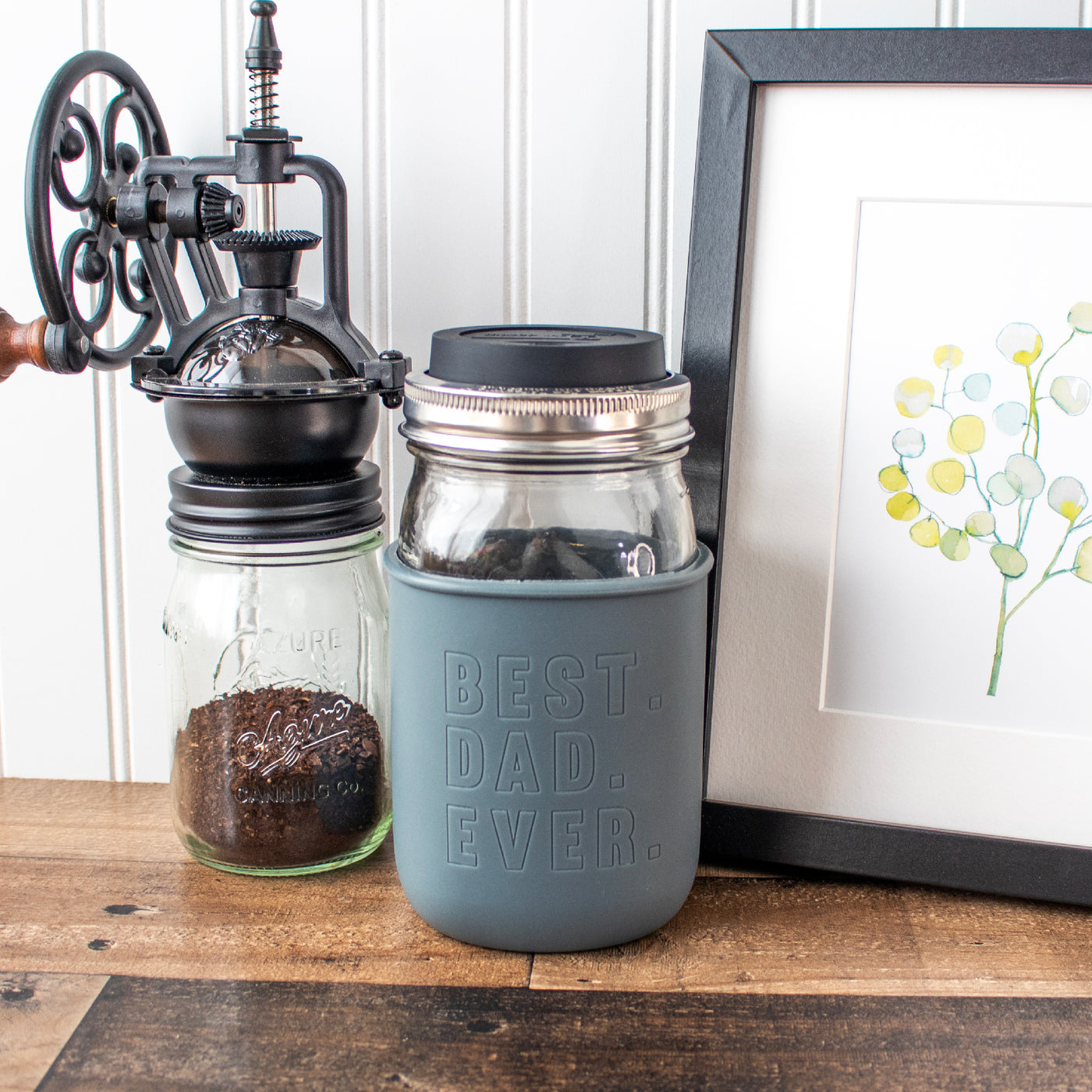 A Mason jar quart jar with the Dad charcoal gray quart sleeve, on quart Mason jar, with coffee grounds and picture frame.