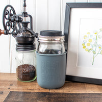 A Mason jar quart jar with the Dad charcoal gray quart sleeve, on quart Mason jar, with coffee grounds and picture frame.