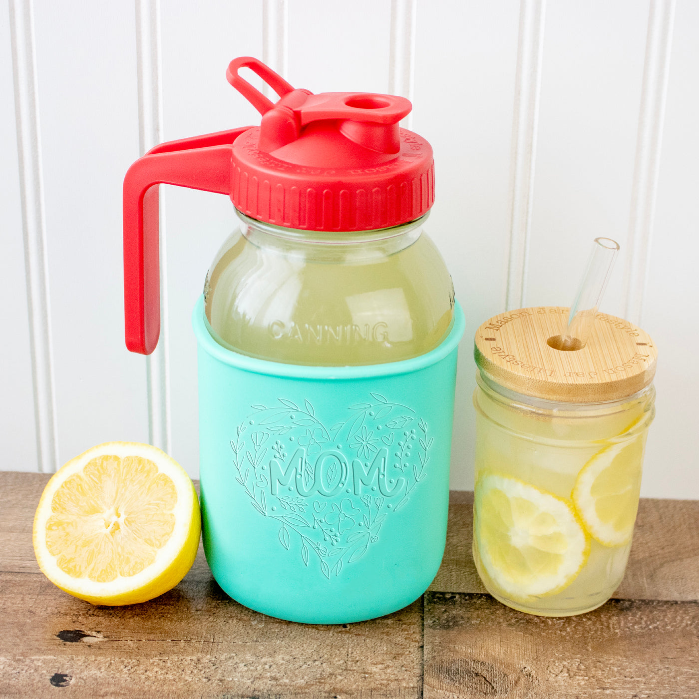 A Mason jar quart jar with the Mom's sleeve and a pitcher lid. Next to it a Mason jar with a bamboo straw hole lid and glass straw.