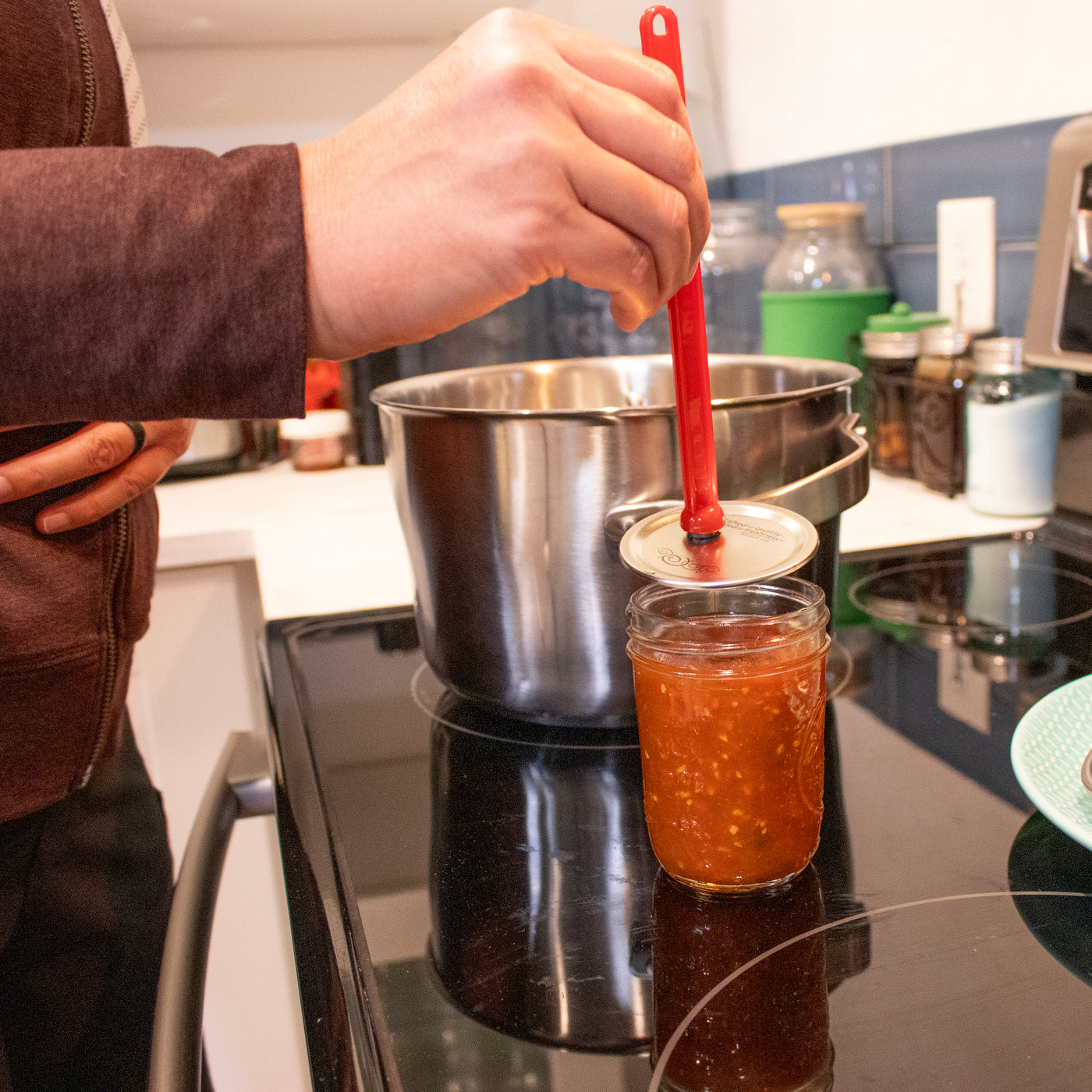 A person holding the lid lifter, and transferring a lid from a boiling pot to a Mason jar, with salsa in it.