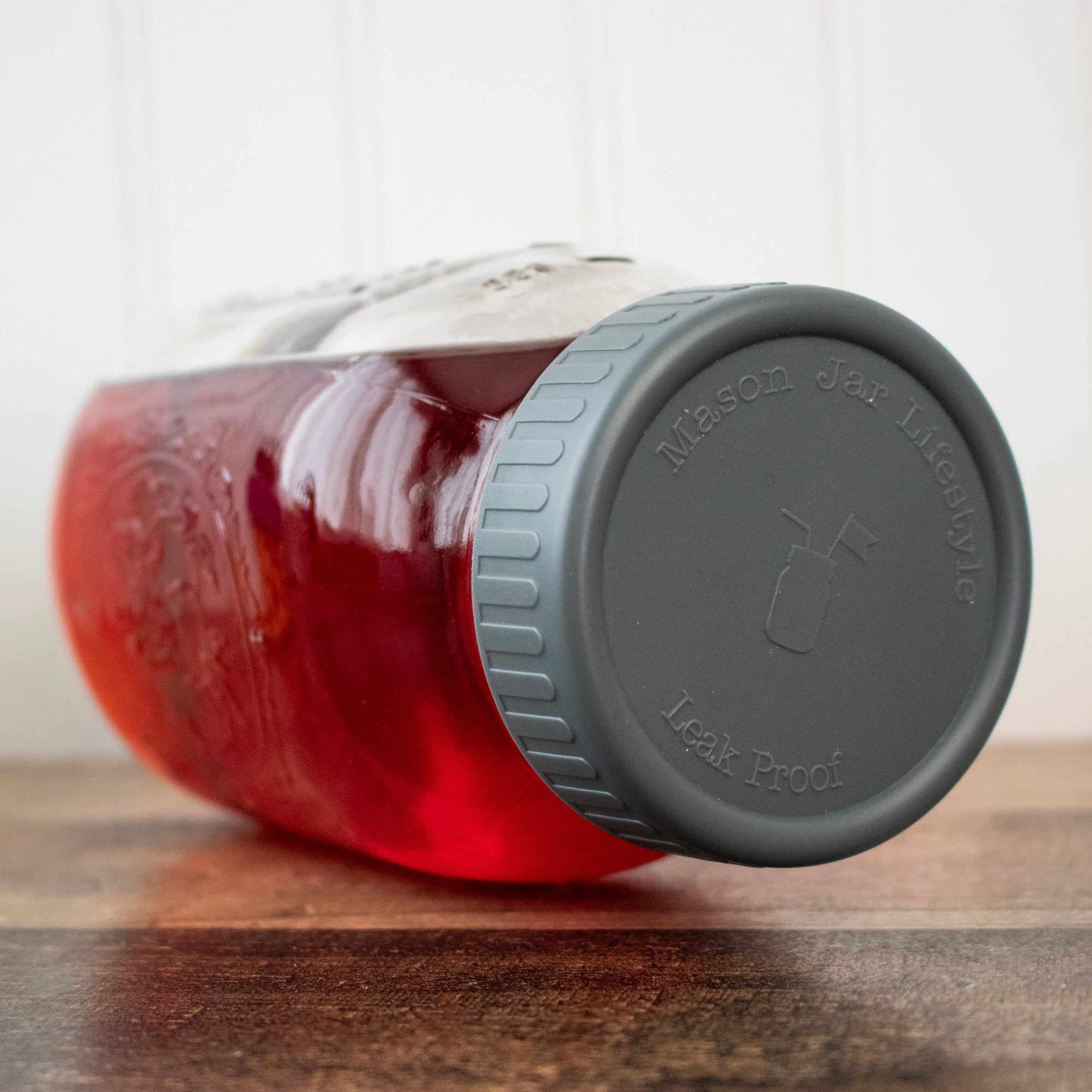A Mason jar tipped on its side with red liquid inside, with a plastic storage lid on it, showing off how leak proof it is.