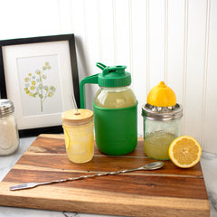 A regular mouth pitcher lid on a quart Mason jar, with lemonade, a juicer, and a mixing spoon fork.