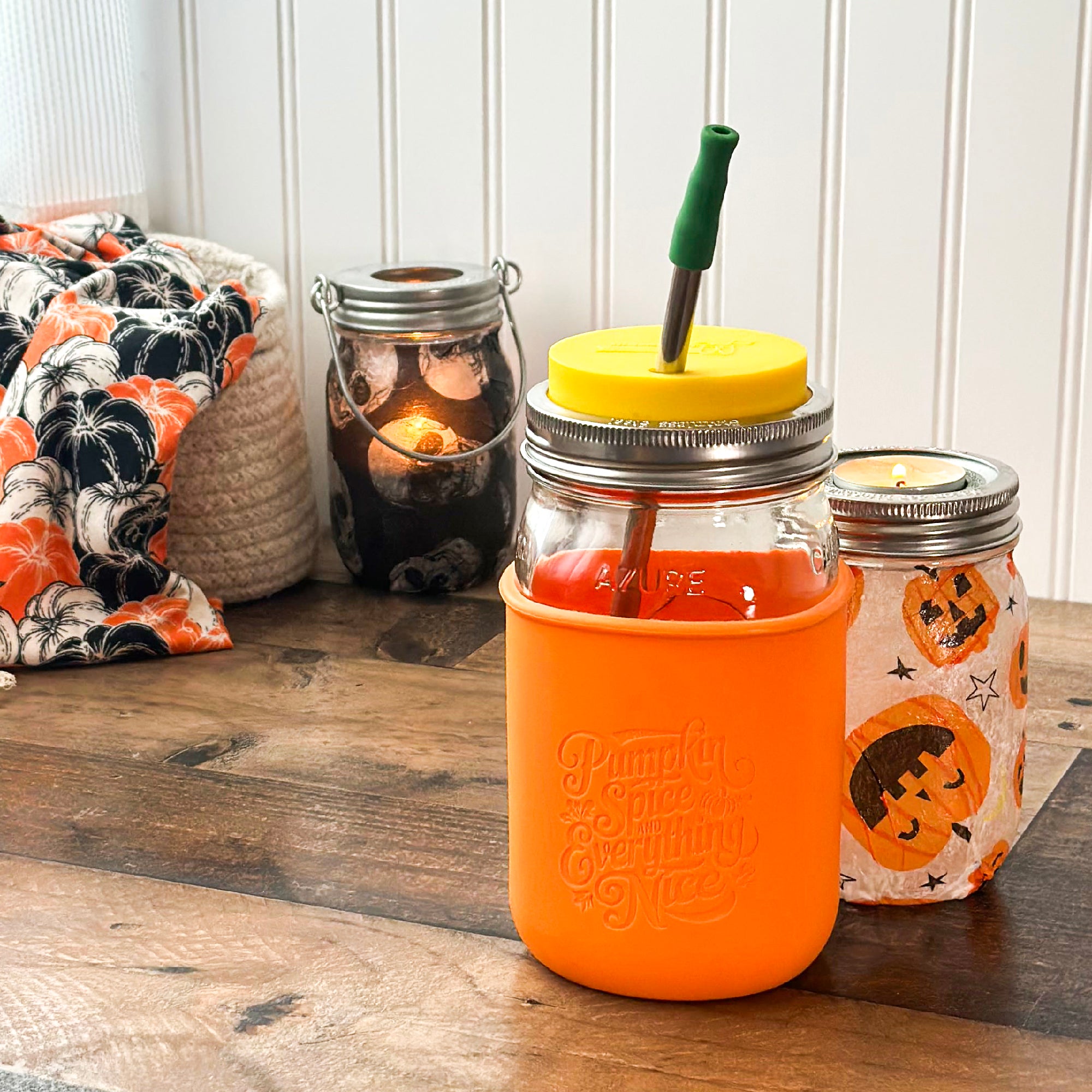 A tangerine colored Mason Jar sleeve on a wide mouth quart 32oz jar, with Halloween and fall decor around it.