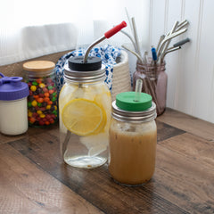 Two different regular mouth Mason jars with silicone straw hole lids on them, with reusable straws.