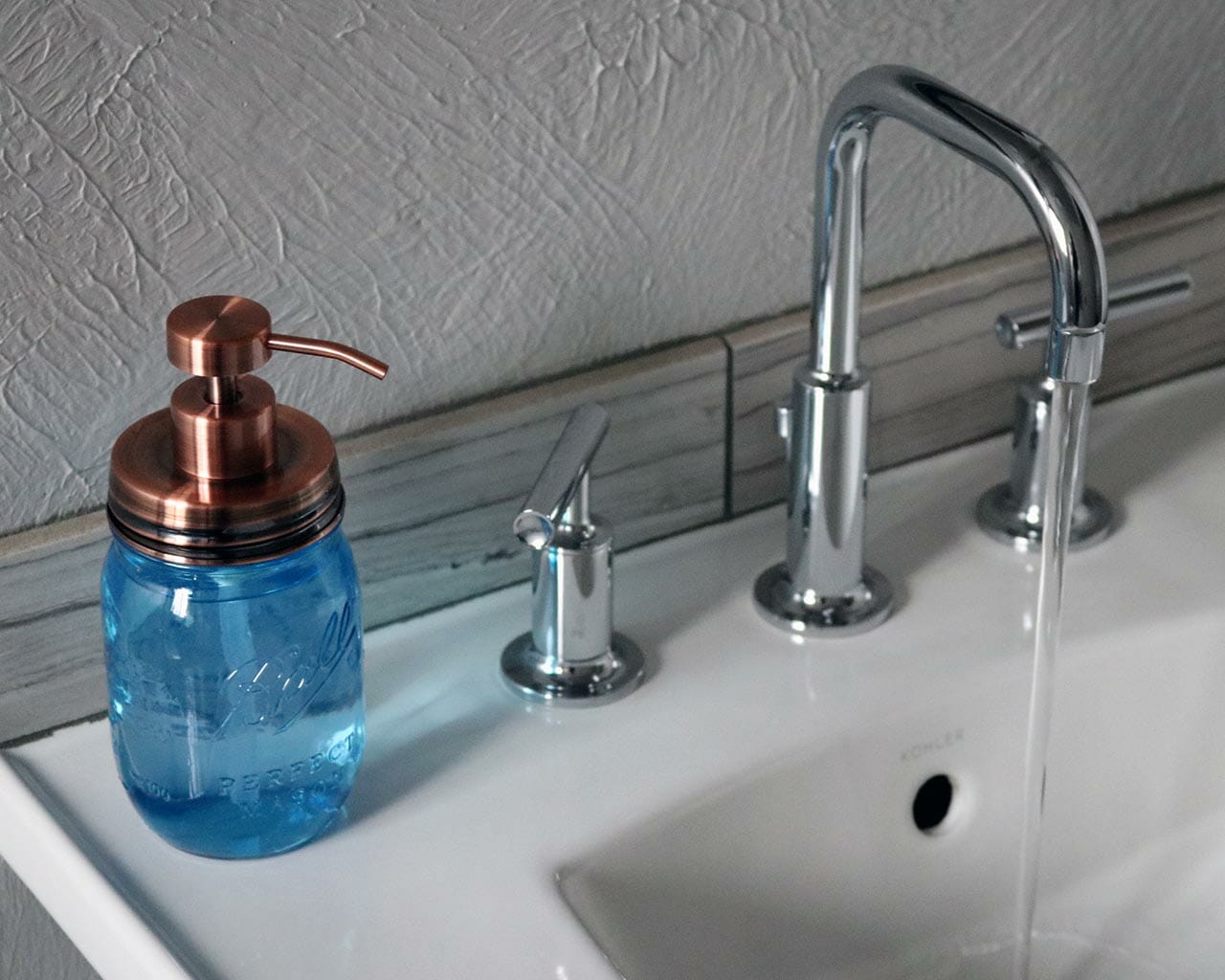 Vintage copper soap pump dispenser lid kit on blue Ball Mason pint jar on sink with running water