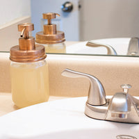 Rose gold soap pump lid on a regular  mouth Mason jar, next to a bathroom sink.