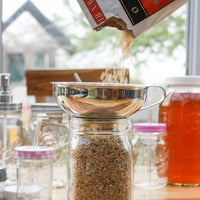 Grains being poured into a metal canning funnel that is sitting on top of a regular mouth quart Mason jar.