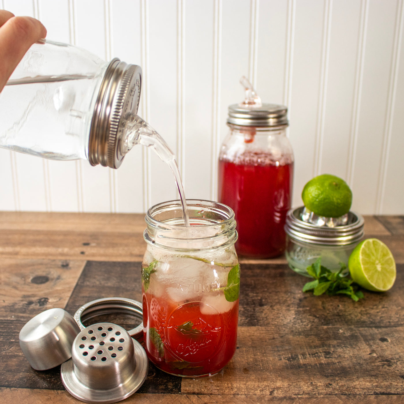 Pieces of the cocktail shaker, next to a drink, with strawberry syrup being poured into it.