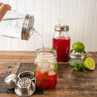 Pieces of the cocktail shaker, next to a drink, with strawberry syrup being poured into it.