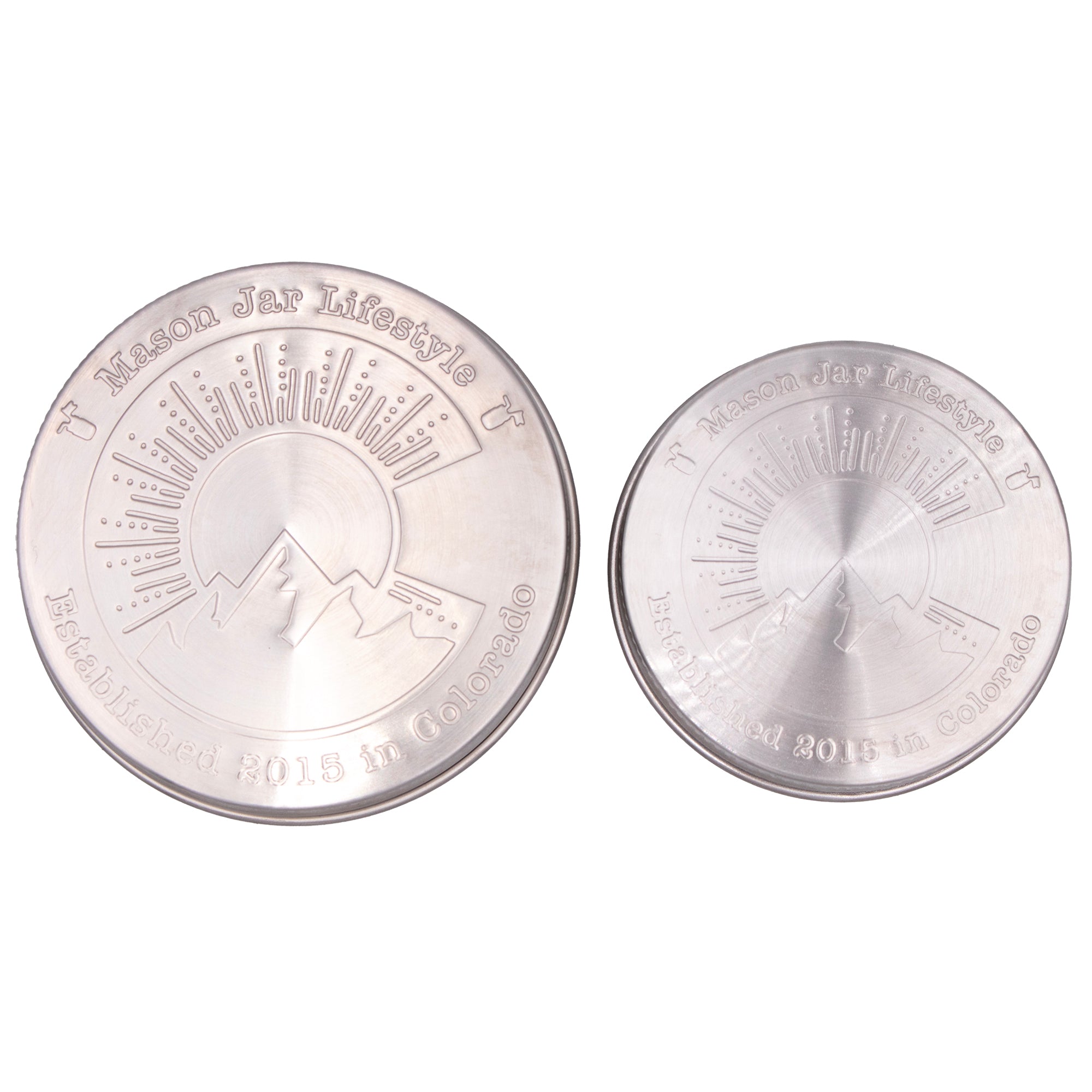 Two stainless steel storage lids for Mason jars up close, showing off the design that says "Mason Jar Lifestyle" and "Established 2015 in Colorado" with a big "C" in the middle with a silhouette of a mountain, a sun, and sun rays.