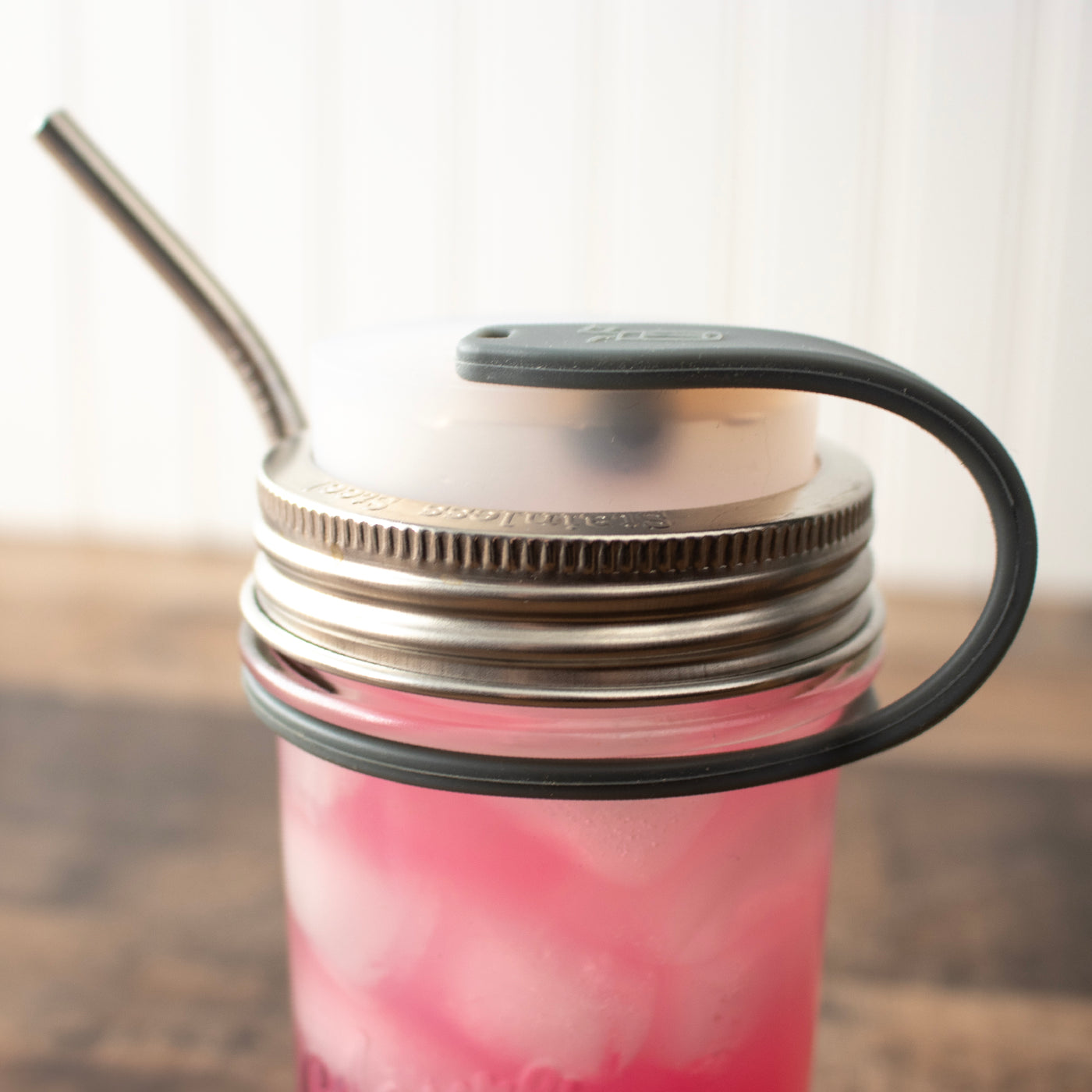 Close up on the silicone straw strap, plugging a straw hole lid and holding a straw along the side of the Mason jar.