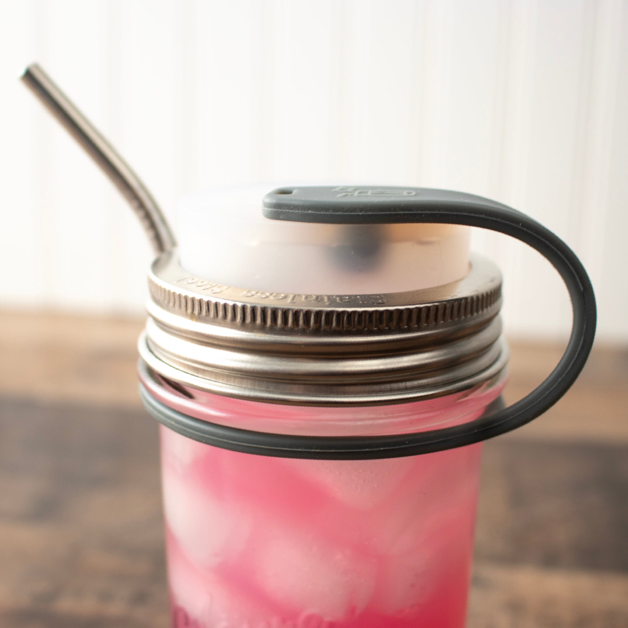 Close up on the silicone straw strap, plugging a straw hole lid and holding a straw along the side of the Mason jar.