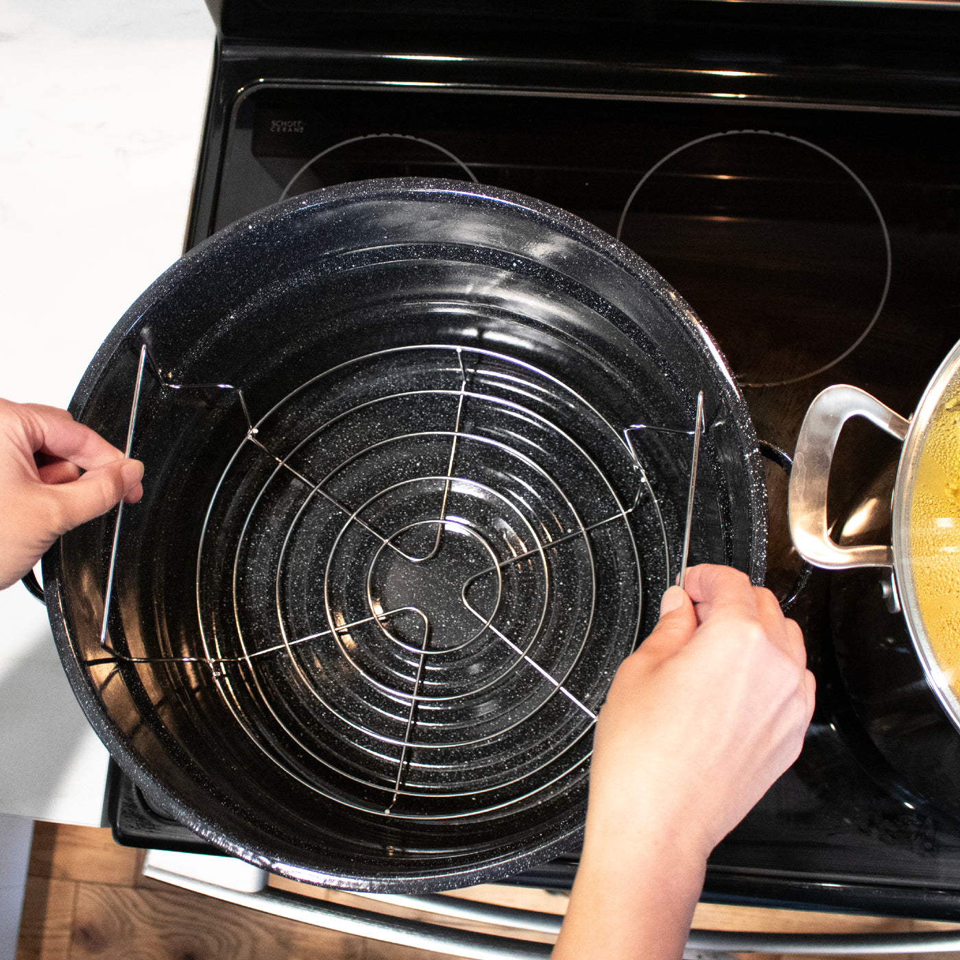 Hand lowering the water canning rack into the pot by it's two handles.
