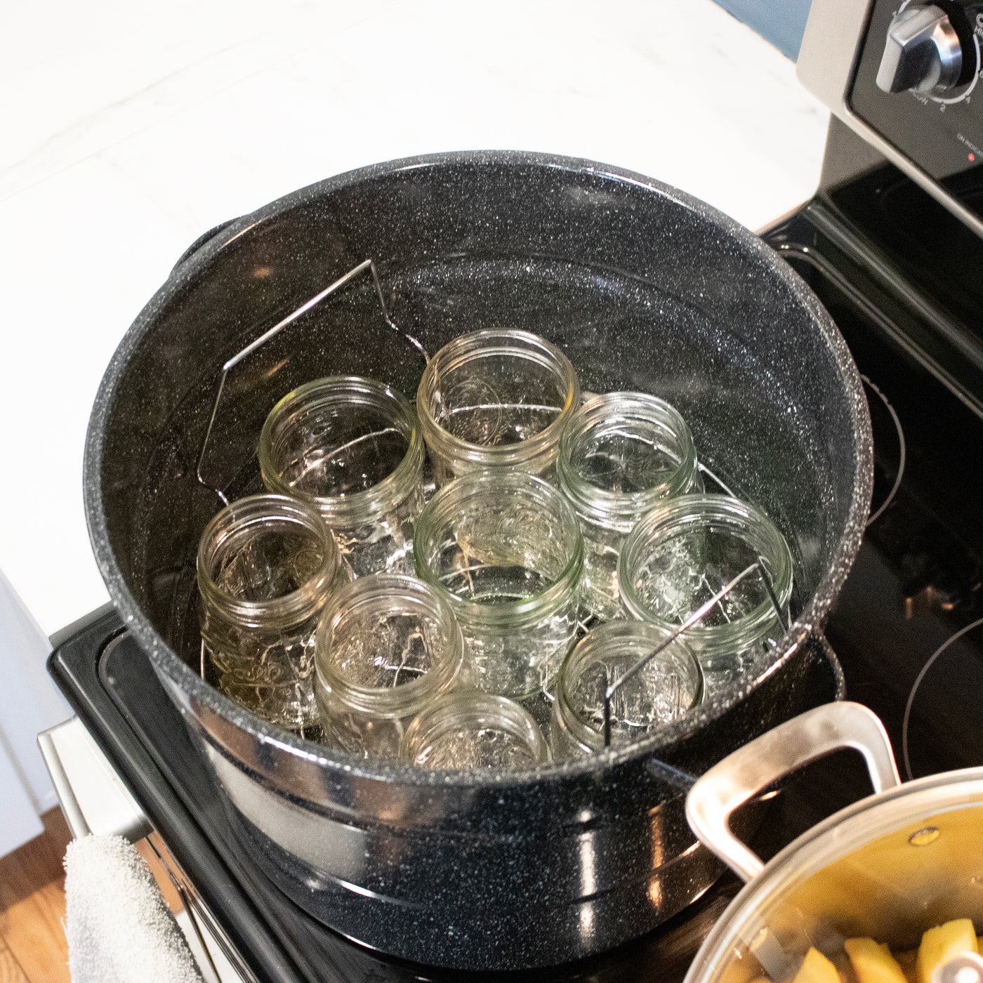 A water canning rack inside of a canning pot, with 9 regular mouth pint Mason jars inside of it.