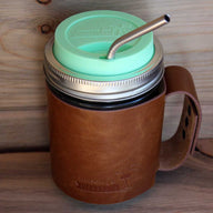 Mint green silicone drinking lid, thin bent stainless steel straw, and faux leather sleeve with handle on wide mouth pint Mason jar