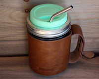 Mint green silicone drinking lid, thin bent stainless steel straw, and faux leather sleeve with handle on wide mouth pint Mason jar