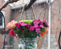 Thin rope handle on wide mouth quart Mason jar with flowers hanging on birch tree