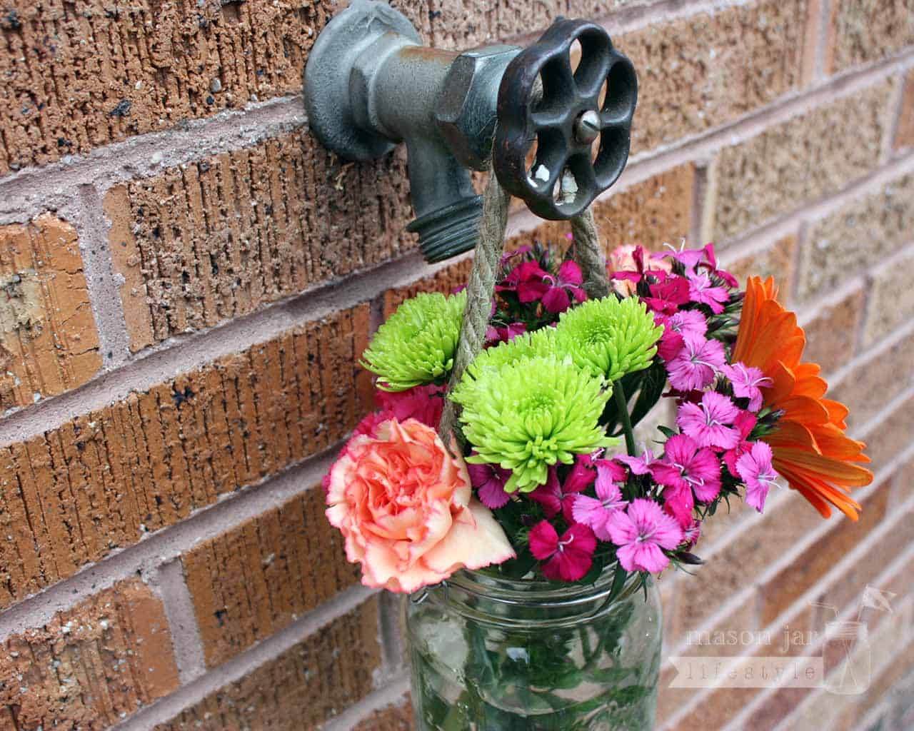 Thin rope handle on wide mouth quart Mason jar with flowers hanging on water faucet