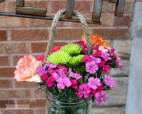 Thin rope handle on wide mouth quart Mason jar with flowers hanging on sign