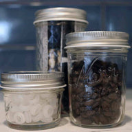 Shiny silver storage lids on 4oz, half pint, and 12oz Ball and Kerr Mason jars with coffee beans and grommets
