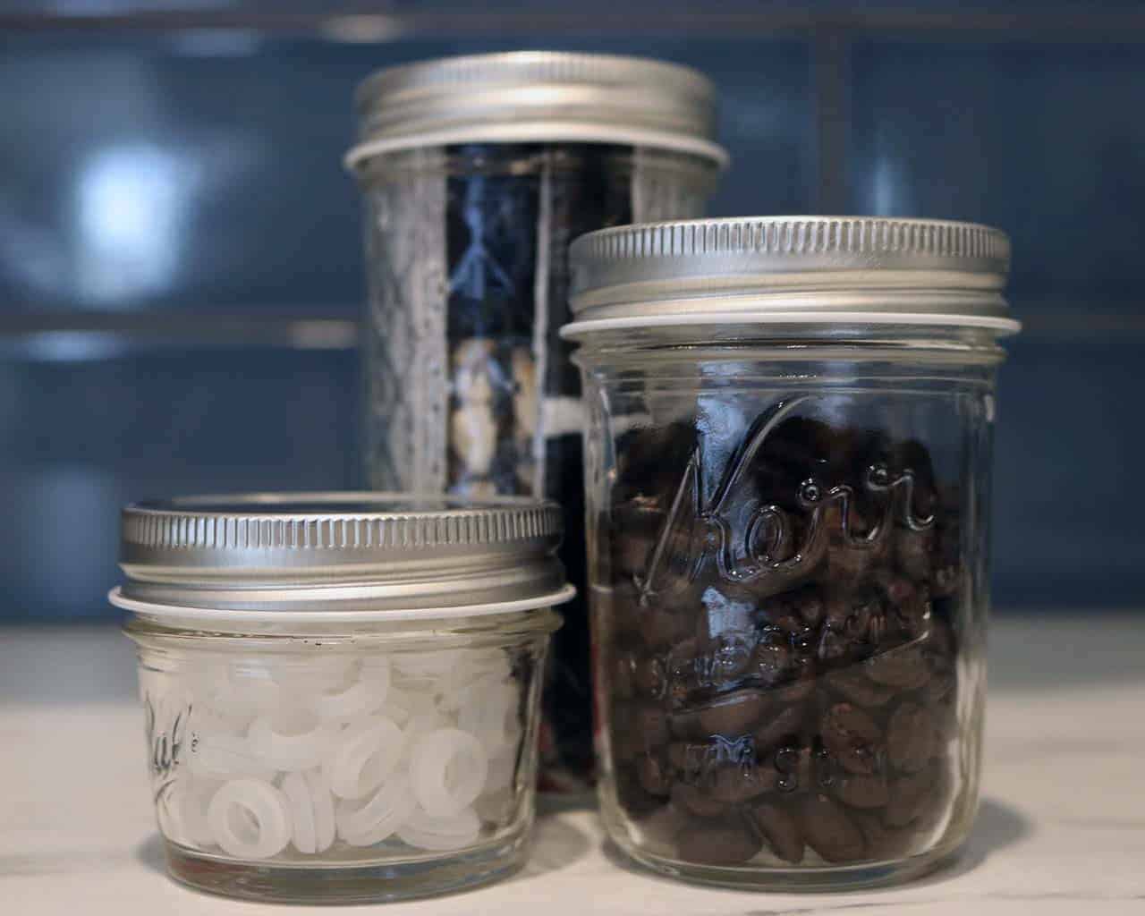 Shiny silver storage lids on 4oz, half pint, and 12oz Ball and Kerr Mason jars with coffee beans and grommets