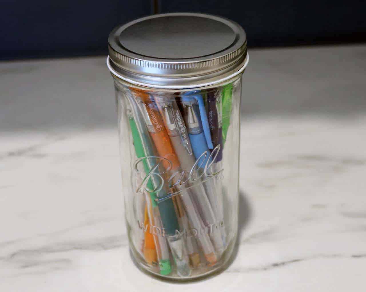Wide mouth shiny silver storage lid on Pint & Half Ball Mason jar with pens
