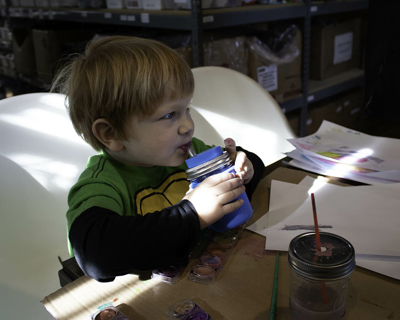 Boy painting and drinking from half pint 8oz Mason jar with silicone straw, sleeve, and lid