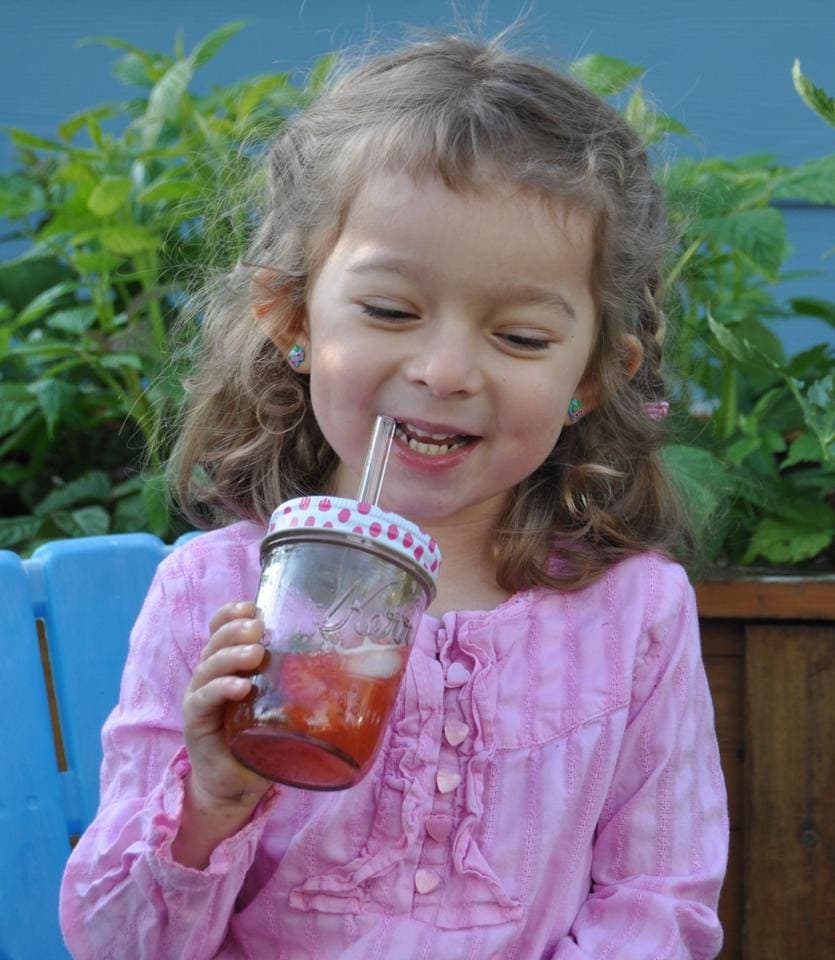 Young girl at a play date drinking from a regular mouth half pint Mason jar with a painted pink polka dot lid and glass straw.
