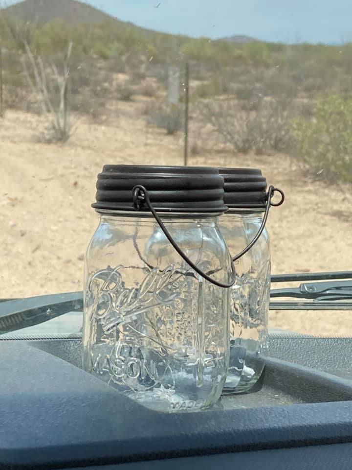 Two regular mouth 16 oz pint Mason jars with solar string lights charging on the dashboard of an RV