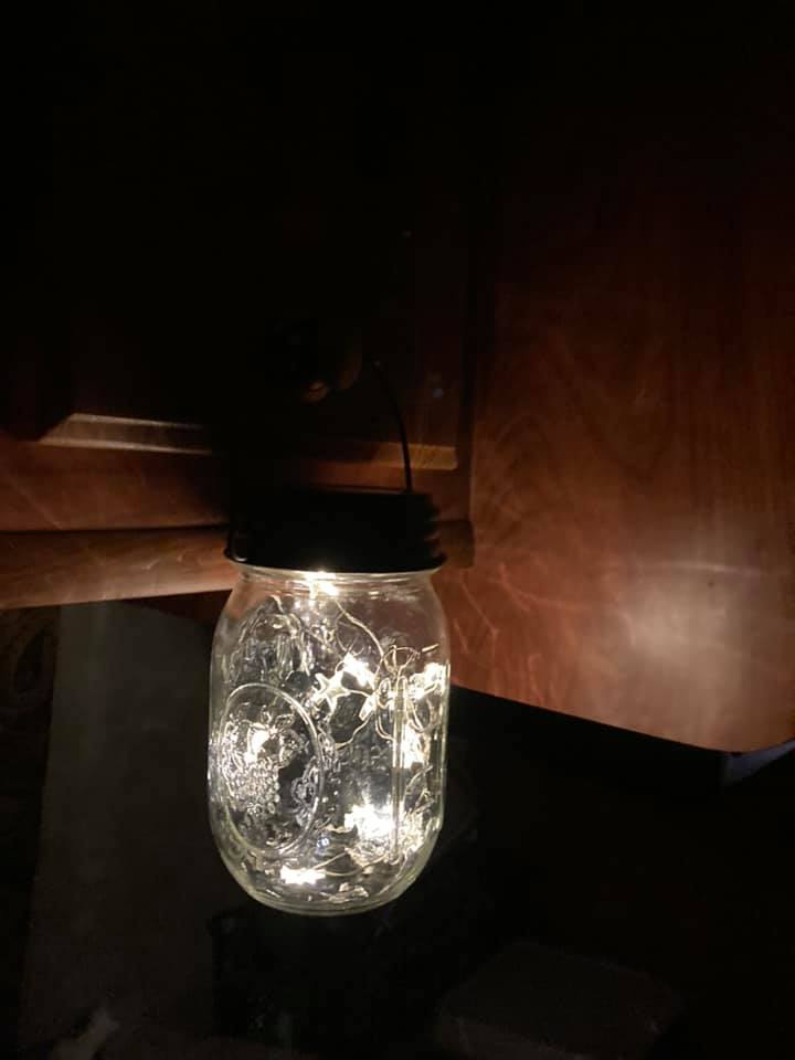 Two regular mouth 16 oz pint Mason jars with solar string lights which were charged on the dashboard of an RV now hanging and glowing