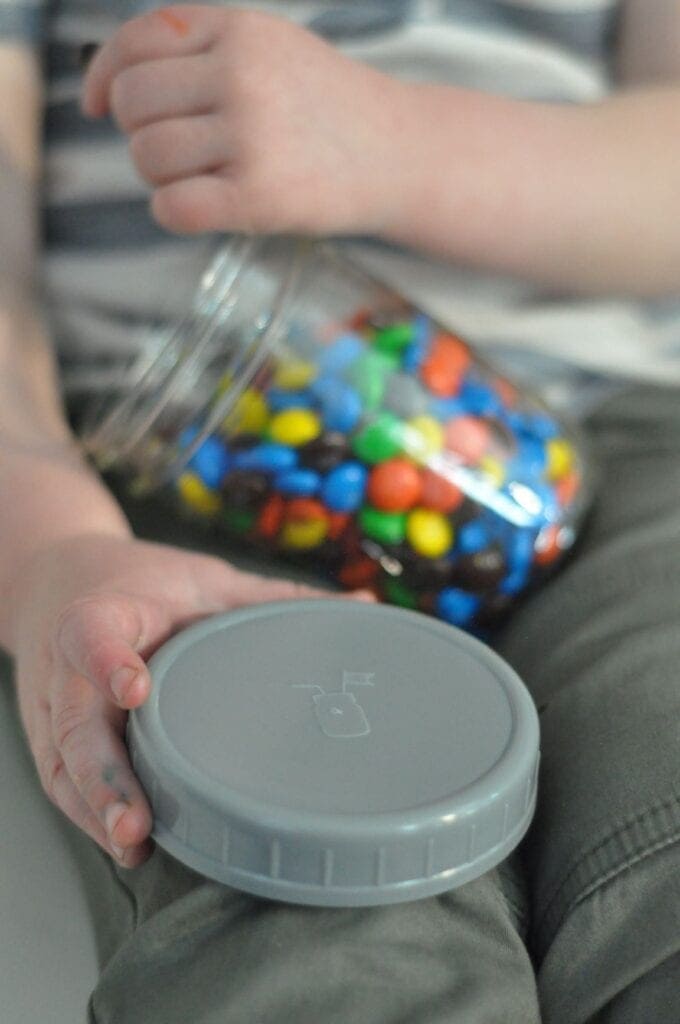 A child holding a Mason Jar Lifestyle gray plastic storage lid with platinum cured silicone liner and a wide mouth Mason jar filled with candy.