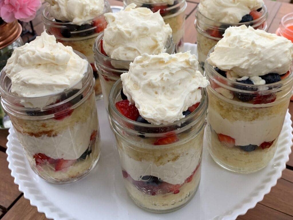 Berry trifle in 8 oz half pint regular mouth Mason jars that are easy to make with simple ingredients like strawberry, blueberry, cream cheese, powered confectioners sugar, pound cake, angel food cake, and whipping cream.