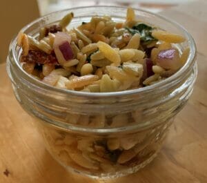 Orzo pasta salad that is easy to make with simple ingredients including tricolor orzo pasta, Italian dressing, spinach, feta cheese, red onion, sun-dried tomatoes in a wide mouth 8 oz half pint Mason jar.