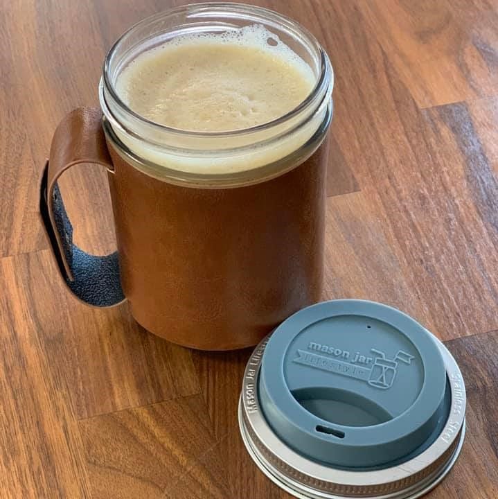 Warm frothy coffee in a wide mouth Ball pint jar ready to go / travel with faux leather sleeve with handle, gray silicone drinking lid, and stainless steel band