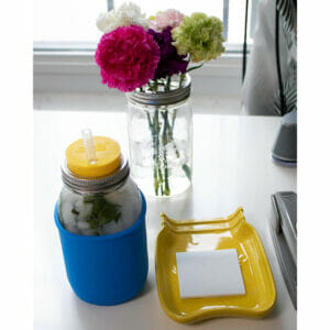 Quart regular mouth mason jar with bright blue silicone sleeve, lemon yellow straw hole, silicone straw, and flowers with frog lid on office desk
